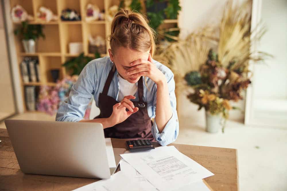 Overwhelmed woman with tax documents and calculator at home, accounting stress.