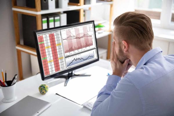 Despairing businessman faced with financial losses sitting at his desk consulting graphs on monitors